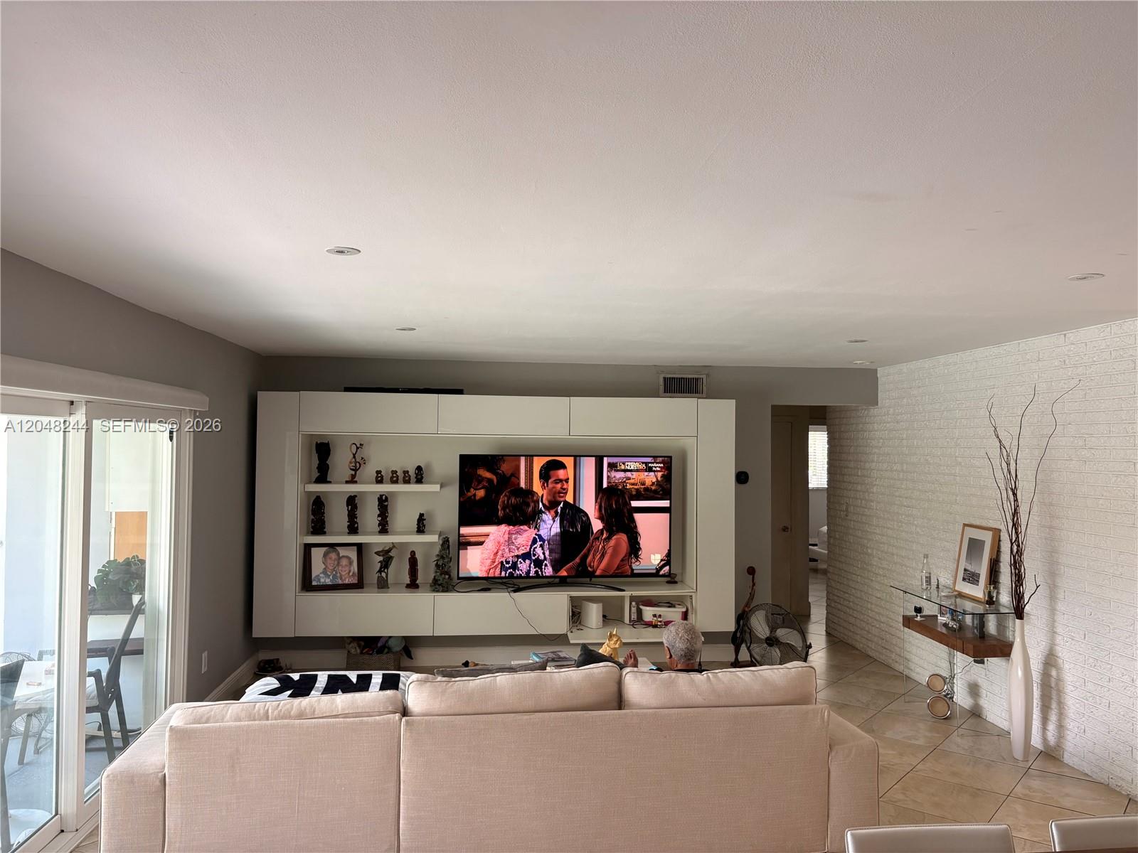 A living room features a large white entertainment center, a beige sofa, and a white brick wall — 12125 NE 2nd Ave, North Miami FL 33161, NORTH MIAMI, FL