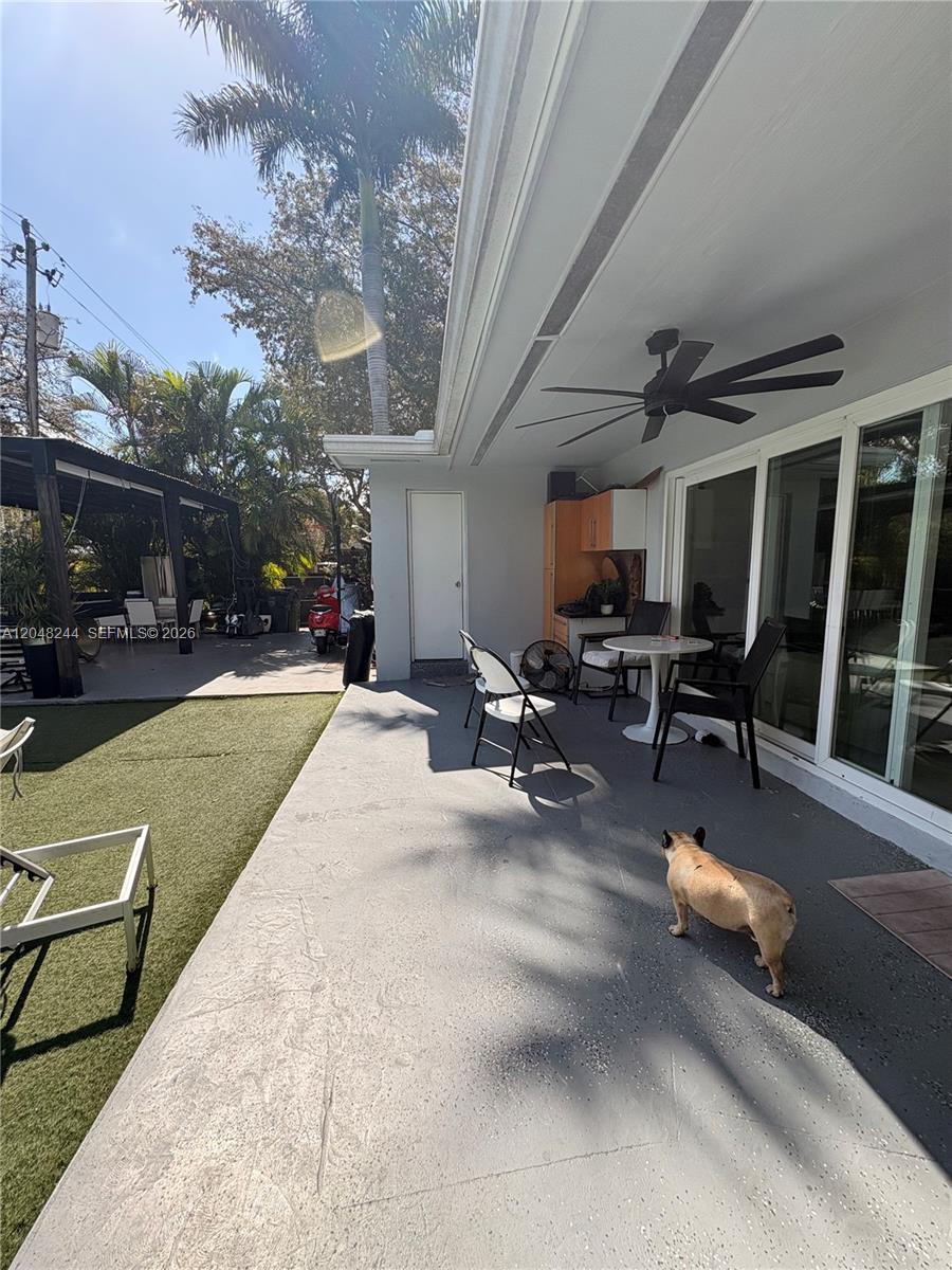 A covered patio features a ceiling fan, outdoor furniture, and a dog on a concrete floor — 12125 NE 2nd Ave, North Miami FL 33161, NORTH MIAMI, FL