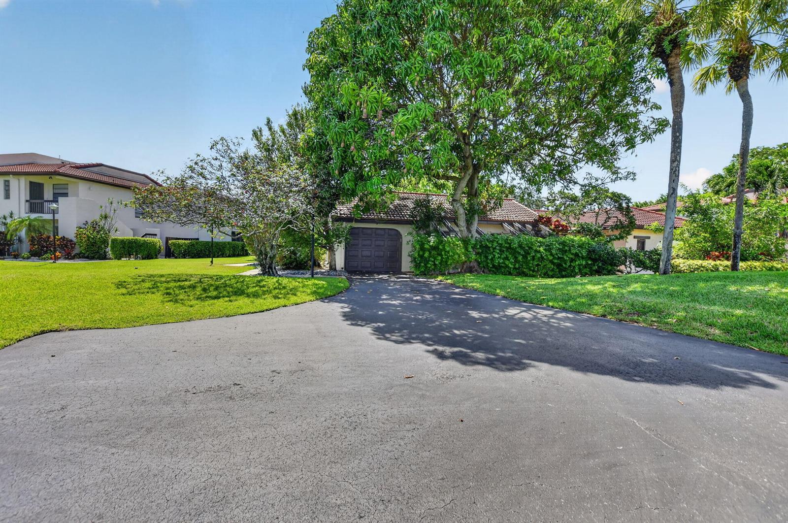 A paved driveway leads to a single-car garage surrounded by lush trees and green lawns — 8208 Casa Del Lago # 23b, Boca Raton FL 33433, BOCA RATON, FL