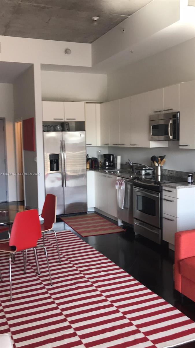 A modern kitchen features stainless steel appliances, white cabinetry, and a red-striped area rug — 2001 Meridian Ave # 426, Miami Beach FL 33139, MIAMI BEACH, FL