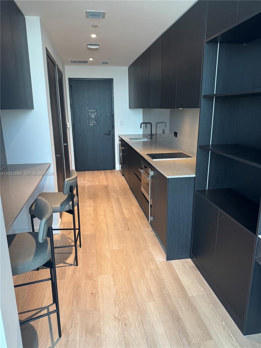 A modern kitchen features dark cabinetry, light countertops, and a built-in breakfast bar with stools — 20 NE 11th St # 3405, Miami FL 33132, MIAMI, FL