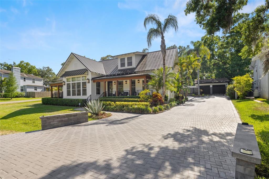 A white farmhouse-style home features a metal roof, a covered porch, and a paved driveway — 5610 N RIVER SHORE DRIVE, TAMPA, FL