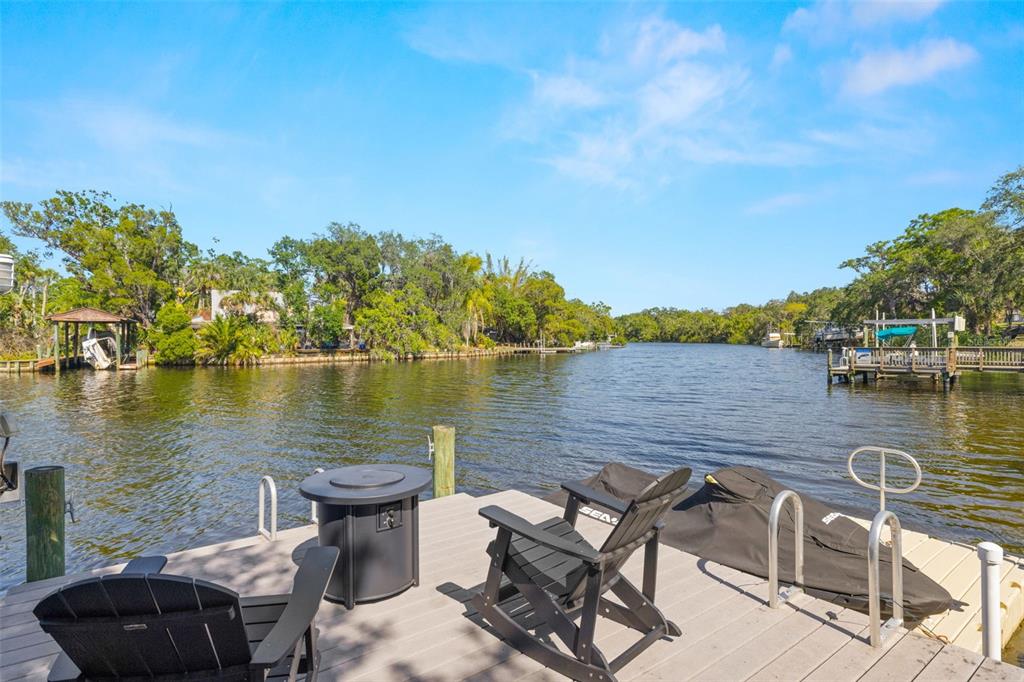 A wooden dock on a river features two chairs, a fire pit, and a jet ski — 5610 N RIVER SHORE DRIVE, TAMPA, FL