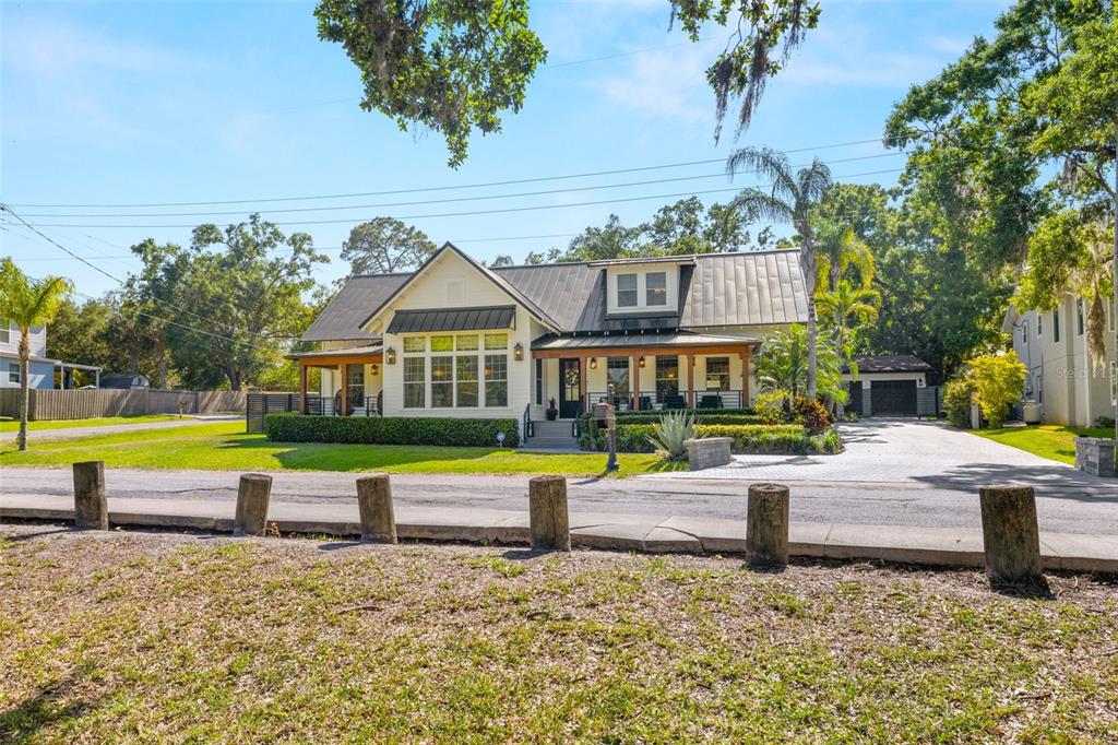 A two-story farmhouse with a metal roof, front porch, and paved driveway sits behind bollards — 5610 N RIVER SHORE DRIVE, TAMPA, FL