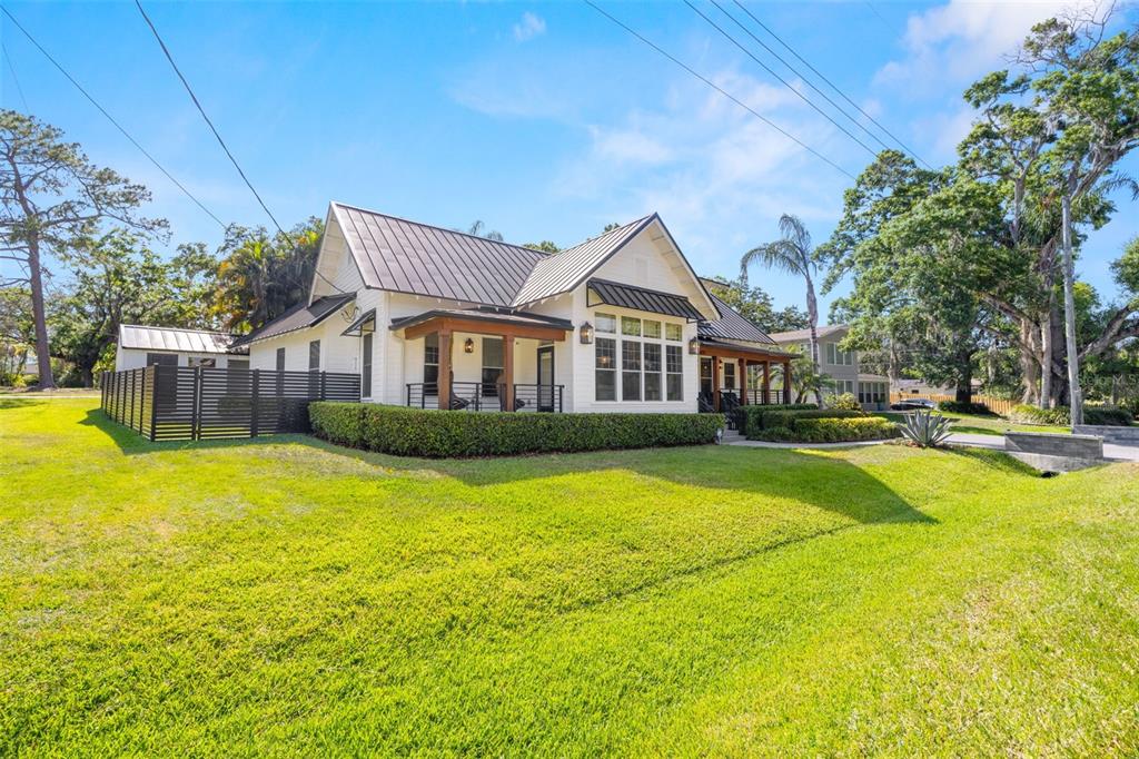 A white house with a dark metal roof and wooden porch accents sits on grass — 5610 N RIVER SHORE DRIVE, TAMPA, FL