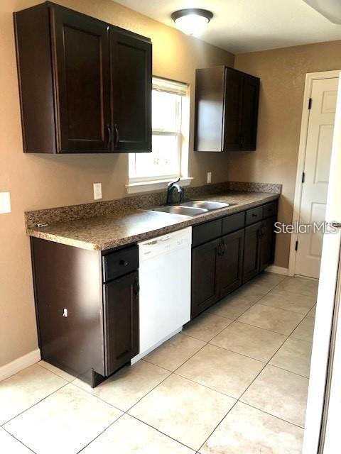 A kitchen features dark wood cabinets, a white dishwasher, and light-colored tile flooring — 16718 SW 21ST CIRCLE, OCALA, FL