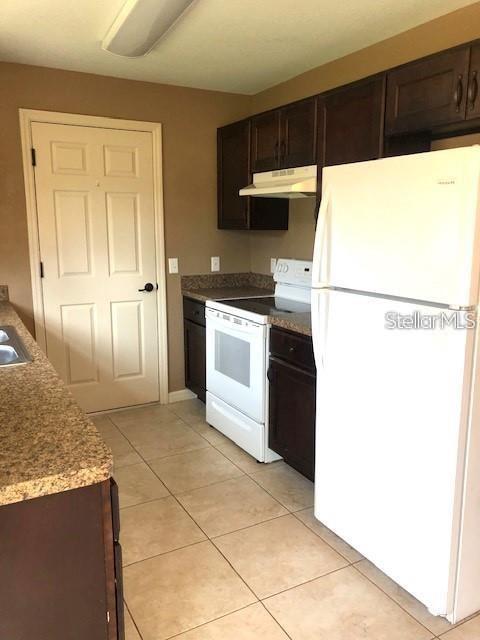 A kitchen features dark wood cabinets, a white refrigerator, a white stove, and tile flooring — 16718 SW 21ST CIRCLE, OCALA, FL