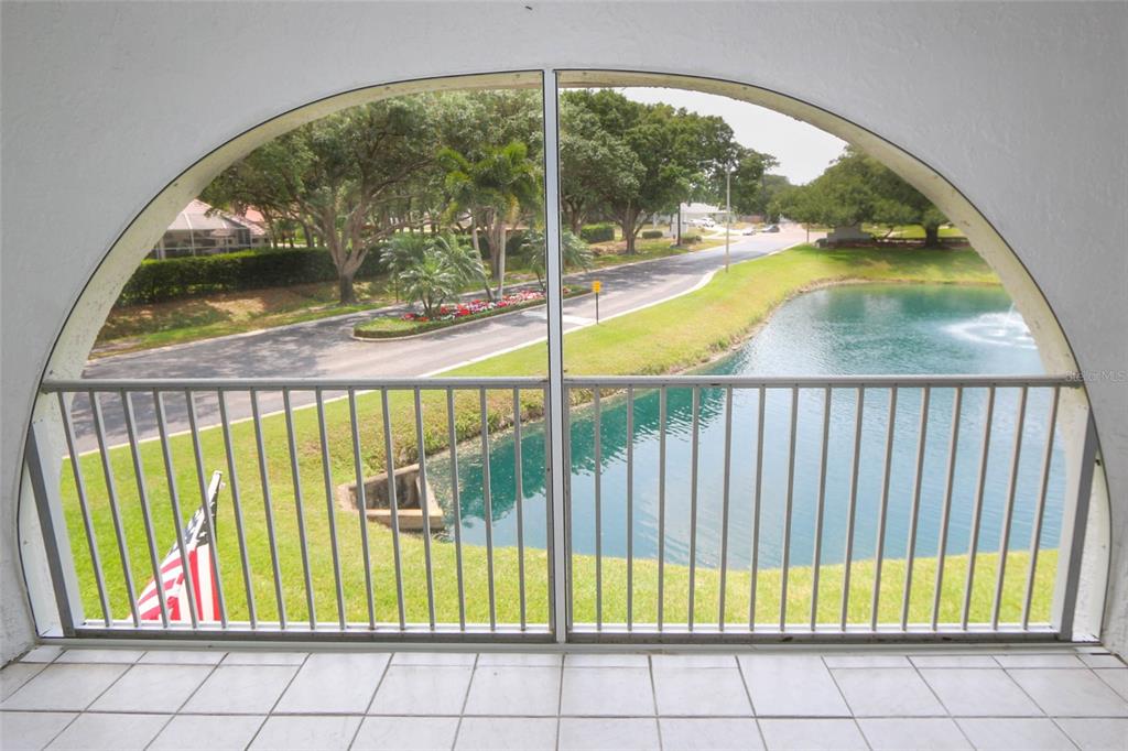 A tiled balcony with a metal railing overlooks a pond, a road, and green trees — 3203 LANDMARK DRIVE UNIT 2202, CLEARWATER, FL