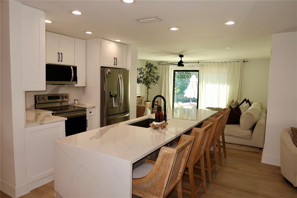 A kitchen features white cabinets, stainless steel appliances, and a large quartz-topped island with seating — 9484 TREASURE LANE NE, ST PETERSBURG, FL