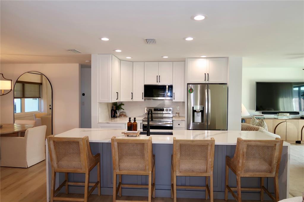 A modern kitchen features white cabinets, a gray island with bar stools, and stainless appliances — 9484 TREASURE LANE NE, ST PETERSBURG, FL