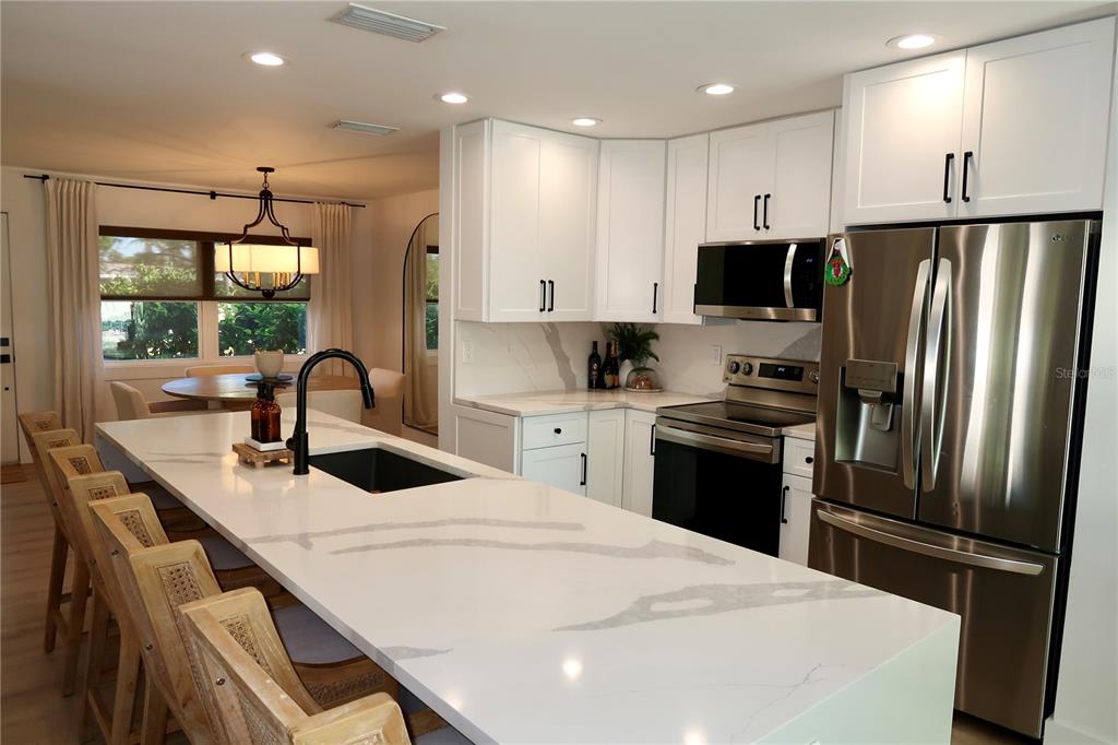 A modern kitchen features white cabinets, a large quartz island, and stainless steel appliances — 9484 TREASURE LANE NE, ST PETERSBURG, FL