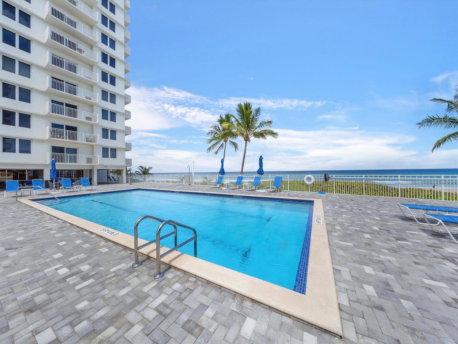 A rectangular swimming pool sits on a paved patio beside a tall white residential building — 3215 S Ocean Boulevard # 104, Highland Beach FL 33487, HIGHLAND BEACH, FL