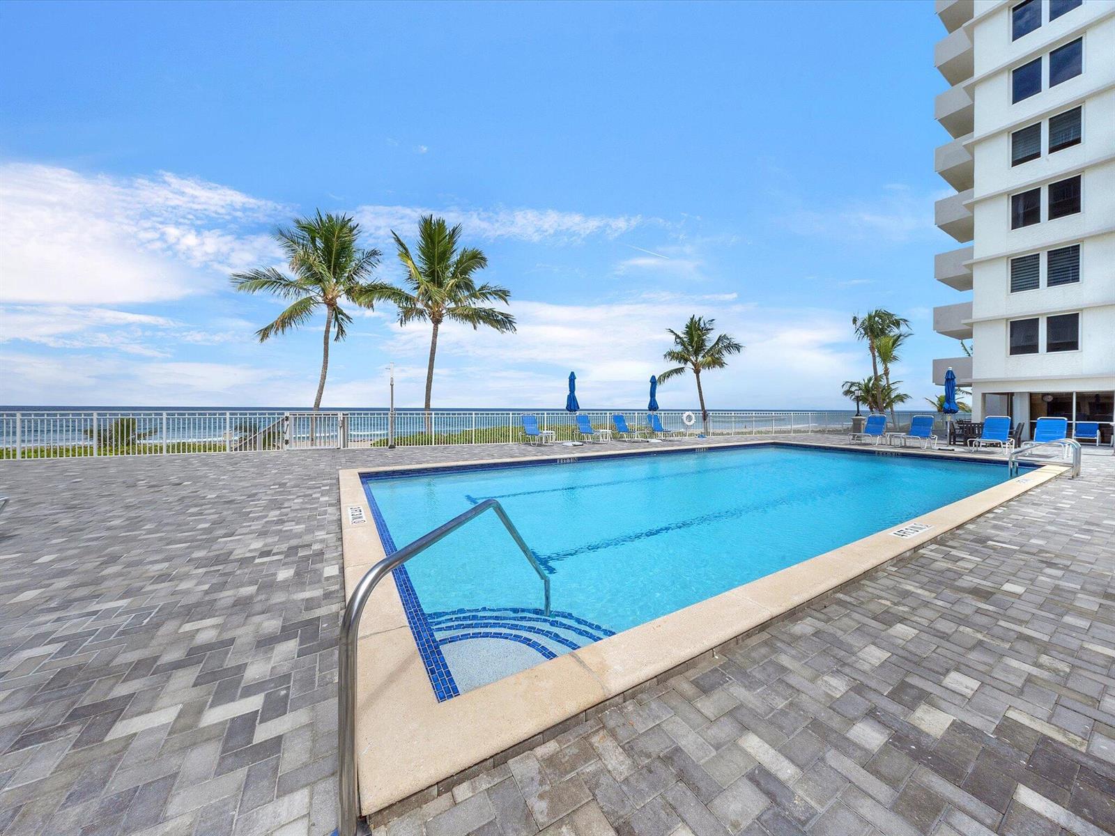 A swimming pool with a metal handrail sits on a paved patio beside a building — 3215 S Ocean Boulevard # 104, Highland Beach FL 33487, HIGHLAND BEACH, FL