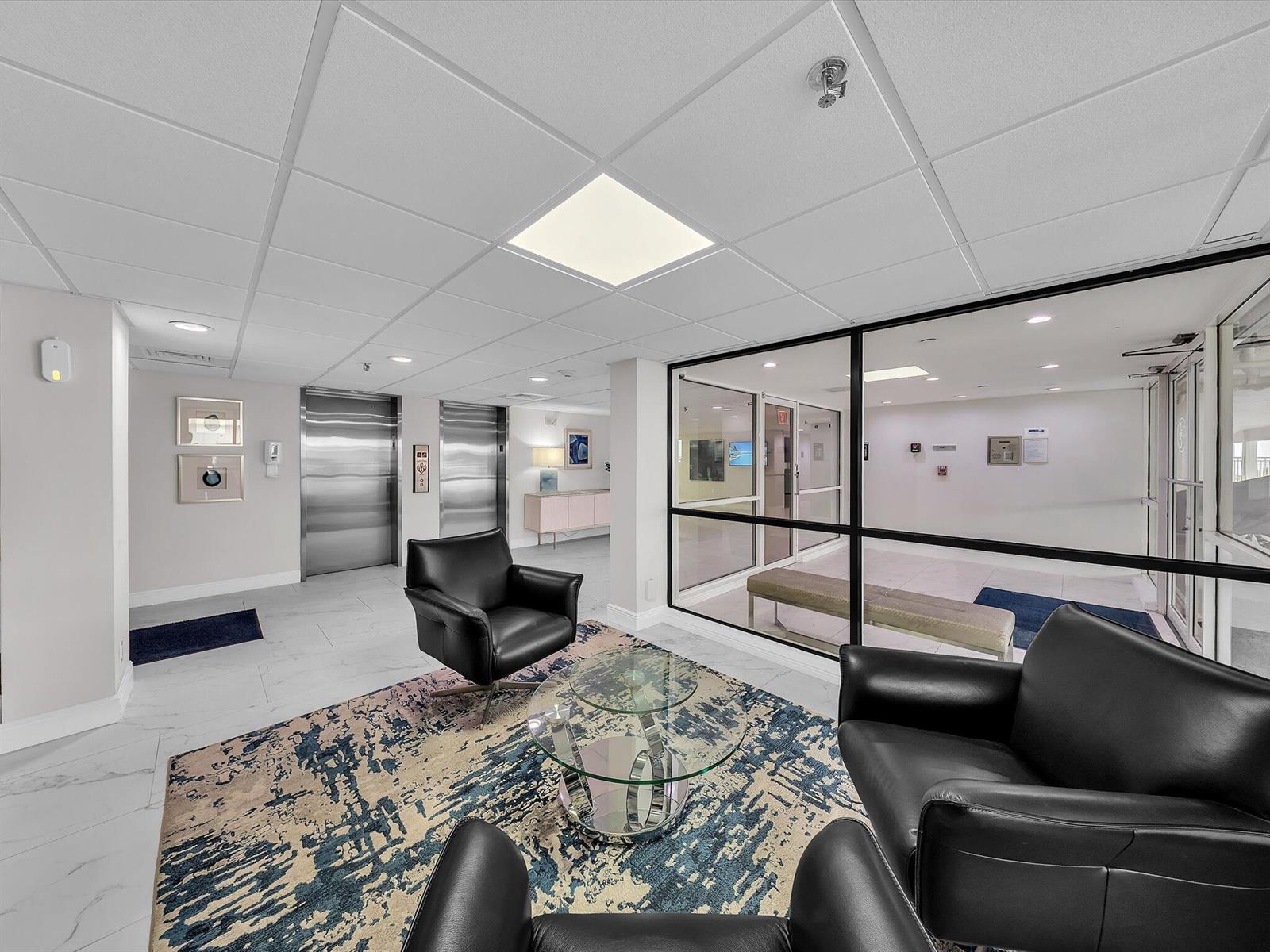 A modern lobby features black leather armchairs, a glass coffee table, and two stainless elevators — 3215 S Ocean Boulevard # 104, Highland Beach FL 33487, HIGHLAND BEACH, FL