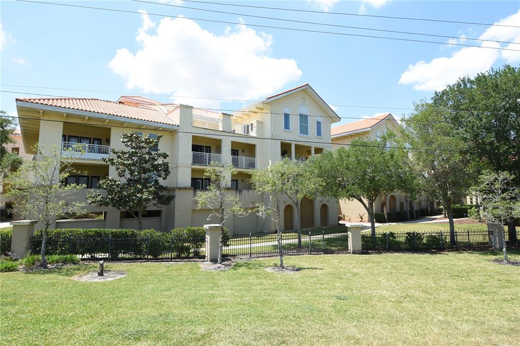 A multi-story apartment building with balconies and a tiled roof sits behind a metal fence — 100 BELLA HARBOR COURT UNIT 111, PALM COAST, FL