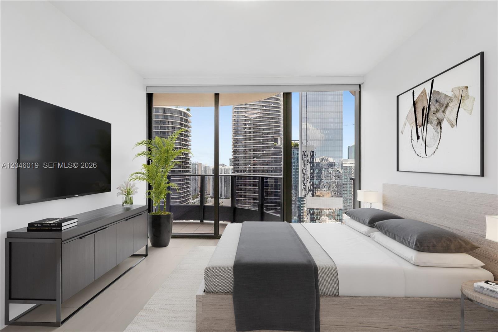 A modern bedroom features a bed, a wall-mounted television, and floor-to-ceiling windows overlooking city buildings — 1000 Brickell Plz # 4015, Miami FL 33131, MIAMI, FL