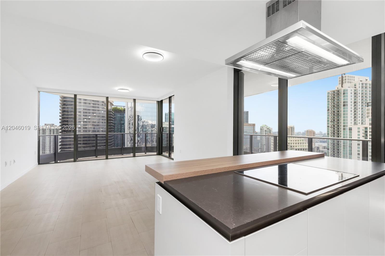 A modern kitchen island with a cooktop overlooks a bright living area with floor-to-ceiling windows — 1000 Brickell Plz # 4015, Miami FL 33131, MIAMI, FL