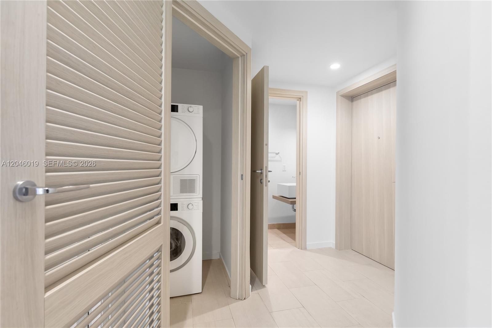 A hallway features light wood-toned doors, tile flooring, and a stacked washer and dryer unit — 1000 Brickell Plz # 4015, Miami FL 33131, MIAMI, FL