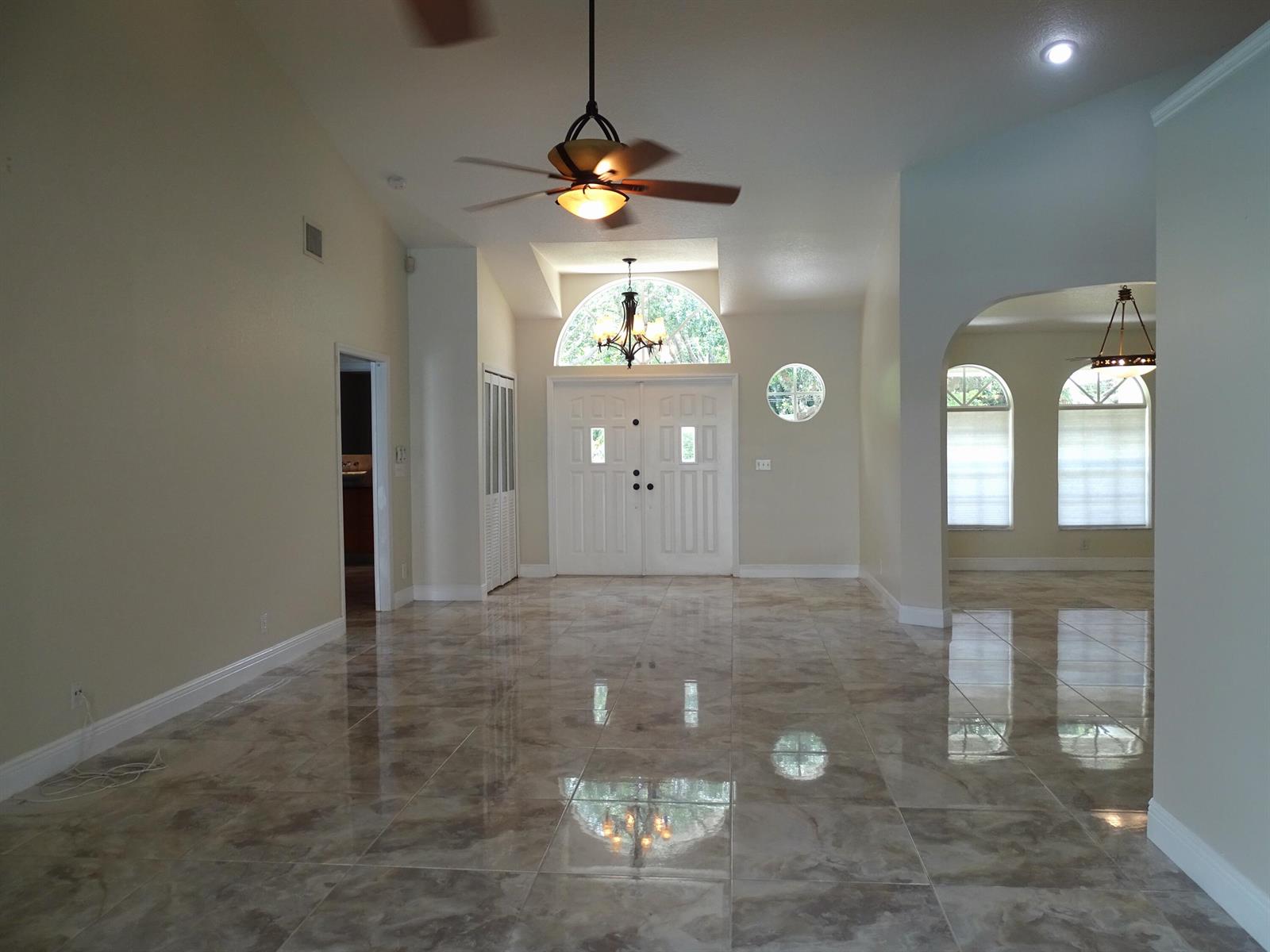 A spacious living room with vaulted ceilings, tile flooring, a ceiling fan, and double entry doors — 6325 Winding Lake Drive, Jupiter FL 33458, JUPITER, FL