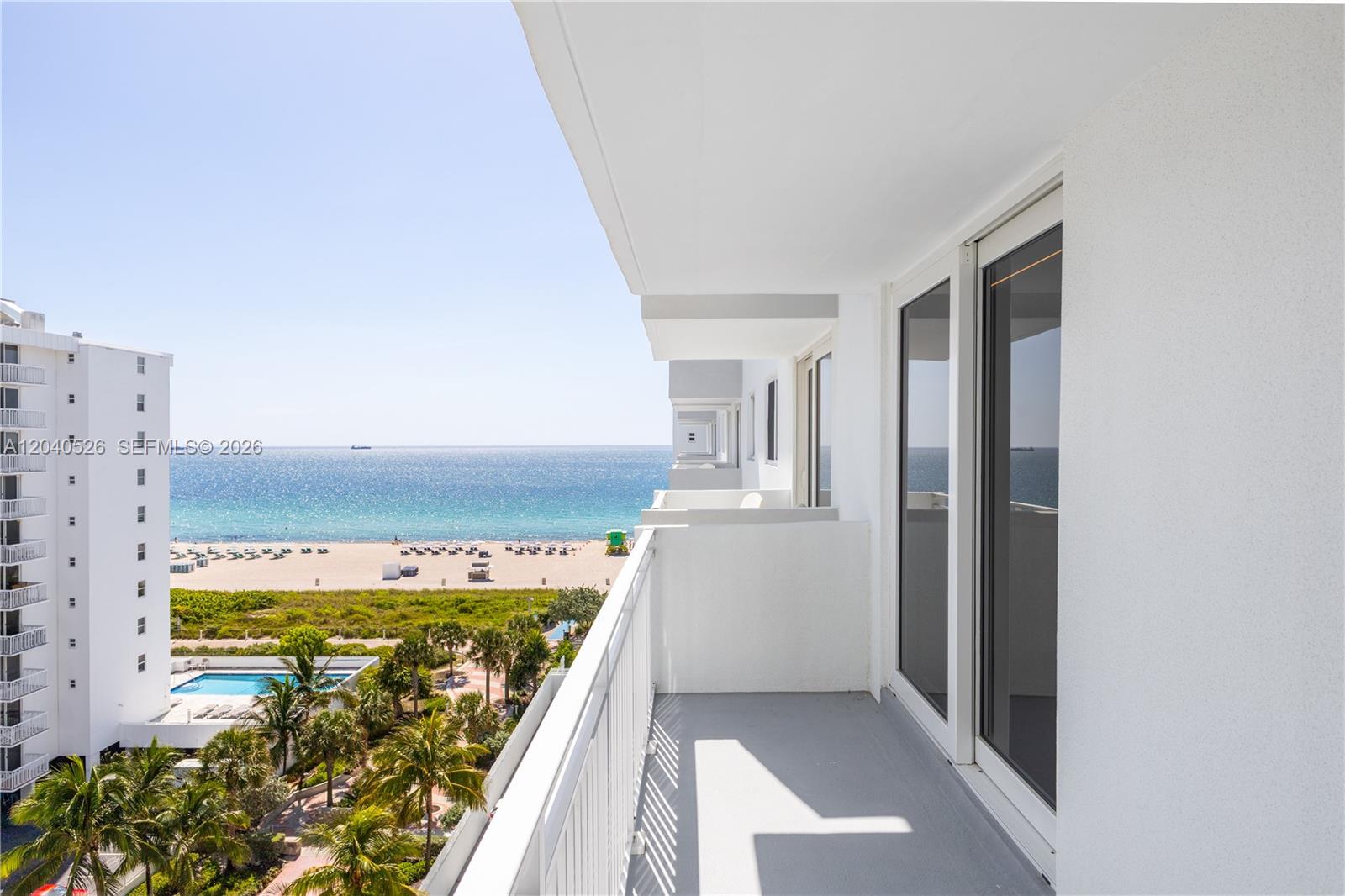 A balcony with a white railing overlooks a beach, ocean, and a swimming pool — 345 Ocean Dr # 924, Miami Beach FL 33139, MIAMI BEACH, FL