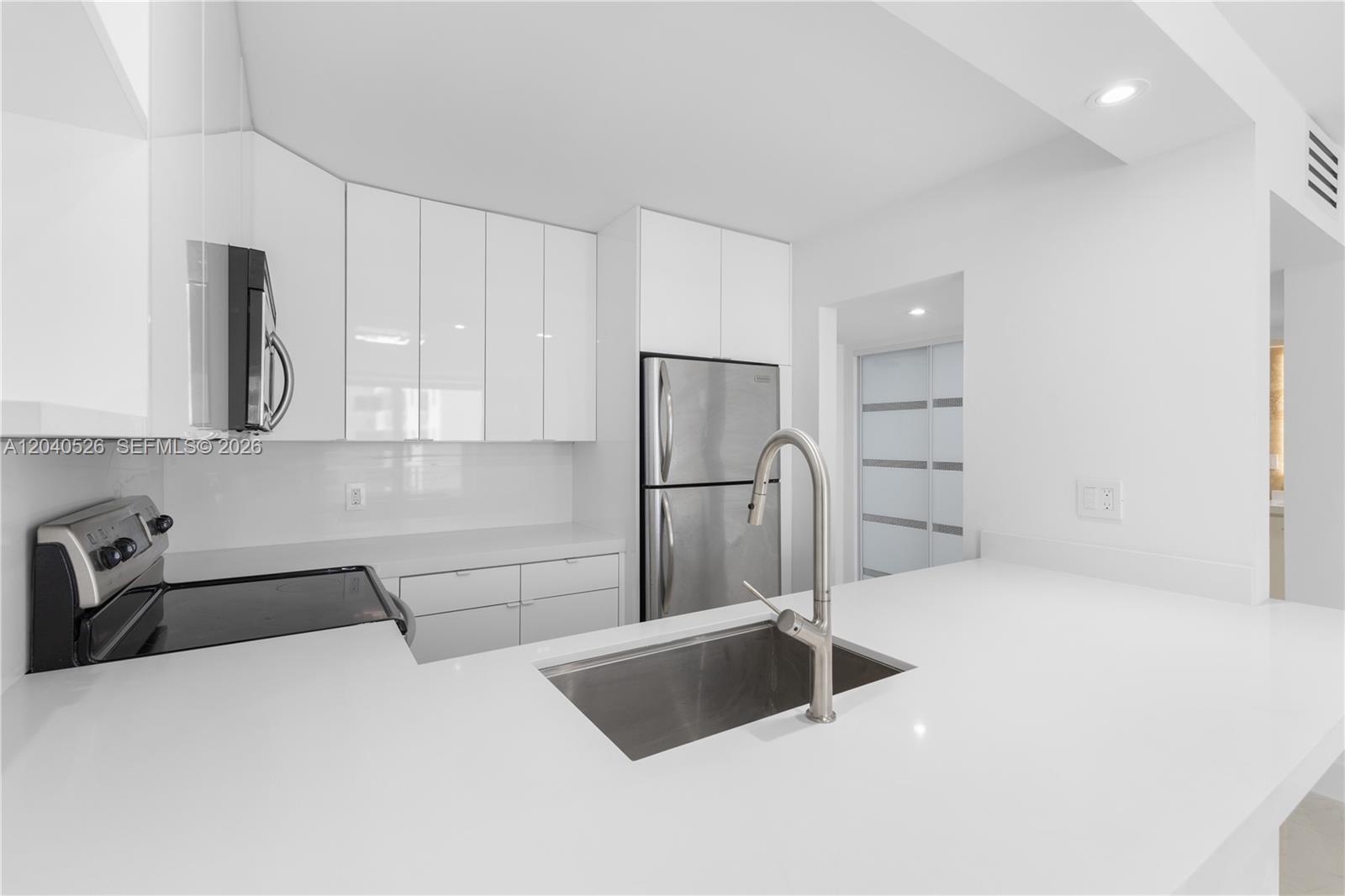 A modern kitchen features white cabinets, stainless steel appliances, and a white countertop — 345 Ocean Dr # 924, Miami Beach FL 33139, MIAMI BEACH, FL