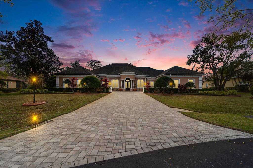 A large, single-story house with a paved driveway and a sunset sky in the background — 8510 KENTUCKY DERBY DRIVE, ODESSA, FL