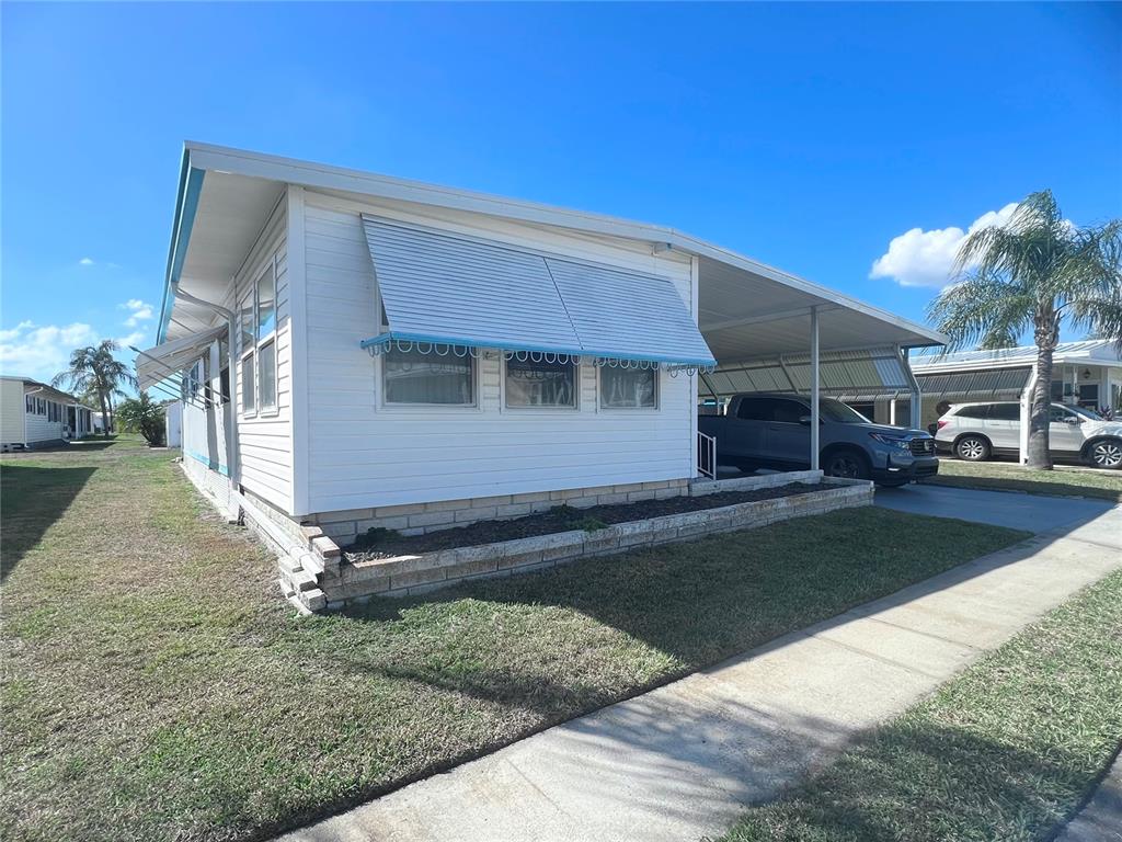 A white mobile home with a carport, metal awnings, and a stone-bordered garden bed — 1100 BELCHER ROAD S UNIT 197, LARGO, FL