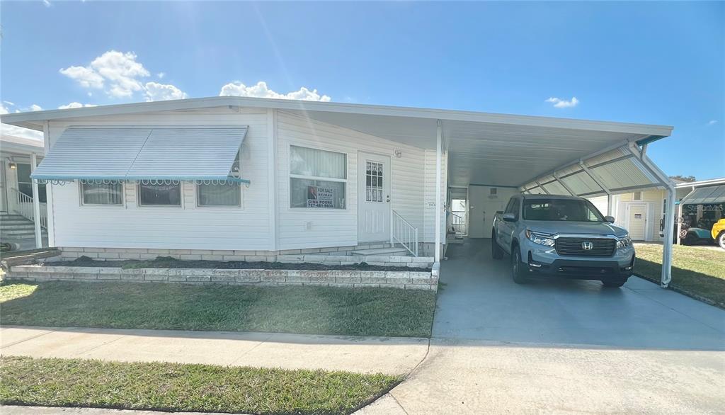 A white mobile home with a carport and a parked pickup truck under a clear sky — 1100 BELCHER ROAD S UNIT 197, LARGO, FL