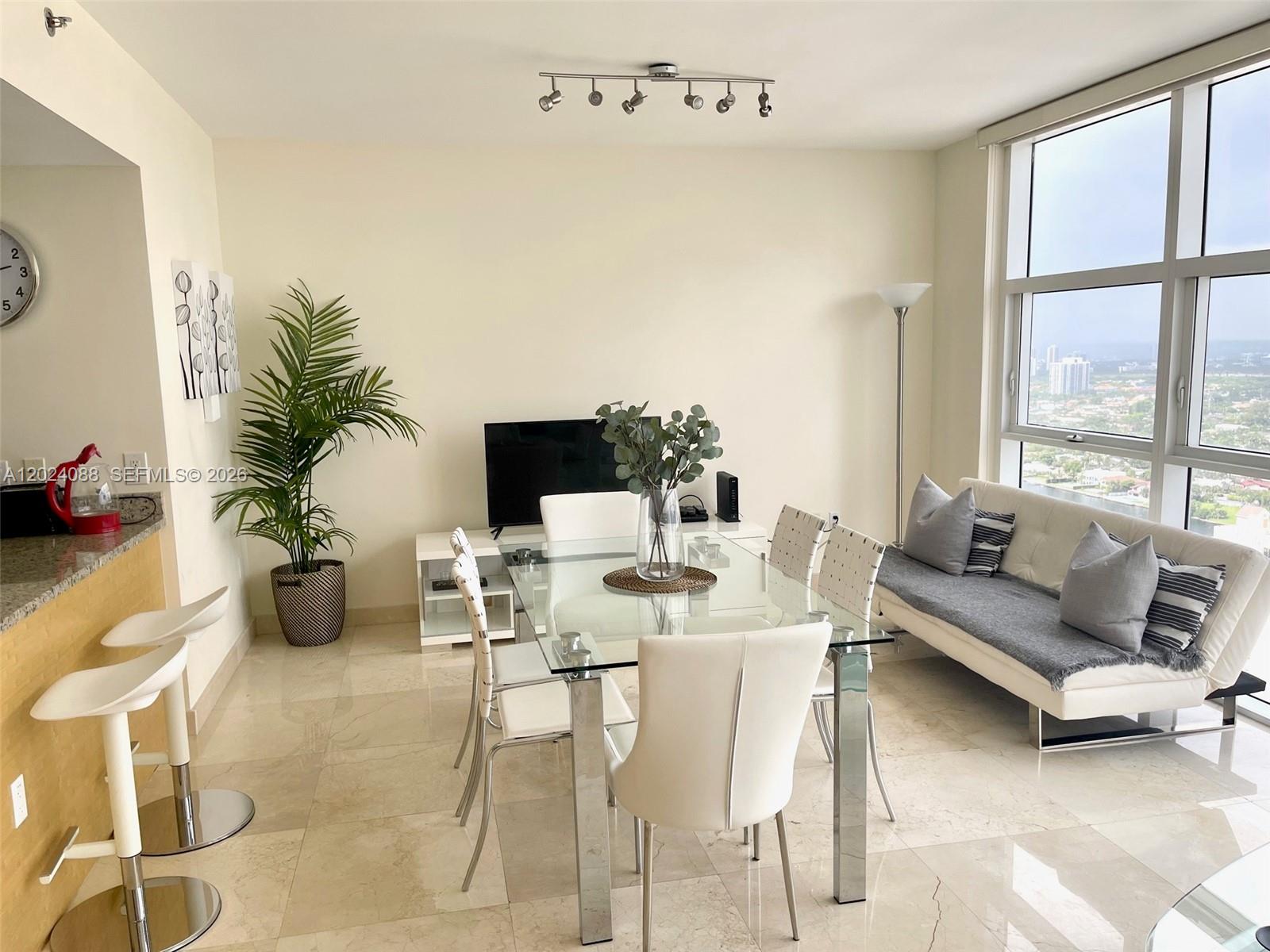 A dining area with a glass table, white chairs, and a sofa near large windows — 1830 S Ocean Dr # 3407, Hallandale Beach FL 33009, HALLANDALE BEACH, FL