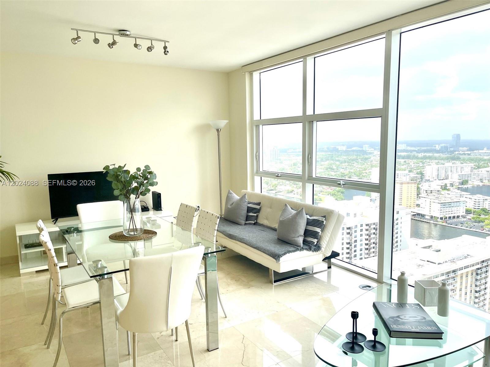 A dining and living area features a glass table, white sofa, and floor-to-ceiling windows — 1830 S Ocean Dr # 3407, Hallandale Beach FL 33009, HALLANDALE BEACH, FL