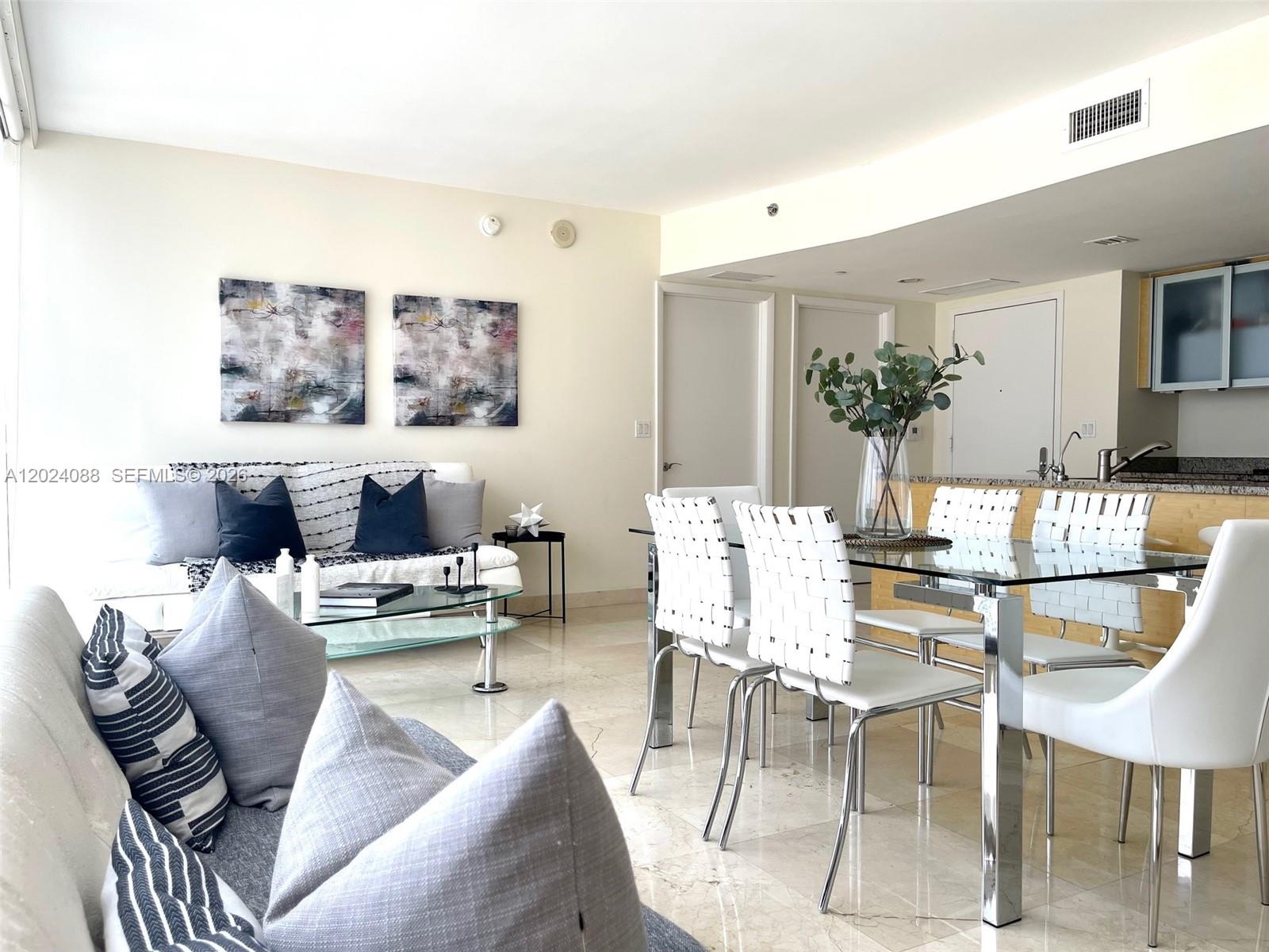 An open-concept living and dining area features a glass table, white chairs, and neutral furniture — 1830 S Ocean Dr # 3407, Hallandale Beach FL 33009, HALLANDALE BEACH, FL