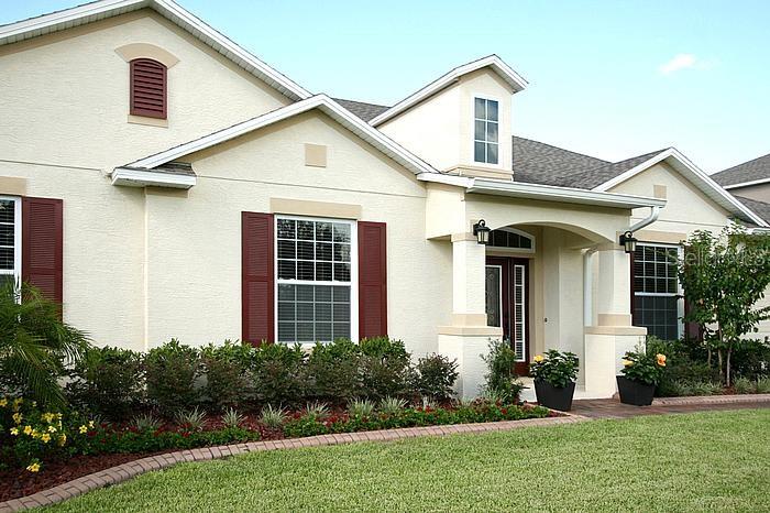 A light-colored suburban house features a front porch, red shutters, and a landscaped yard — 1195 LATTIMORE DRIVE, CLERMONT, FL