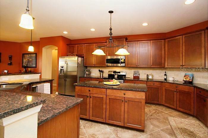 A kitchen features wood cabinets, granite countertops, a central island, and stainless steel appliances — 1195 LATTIMORE DRIVE, CLERMONT, FL