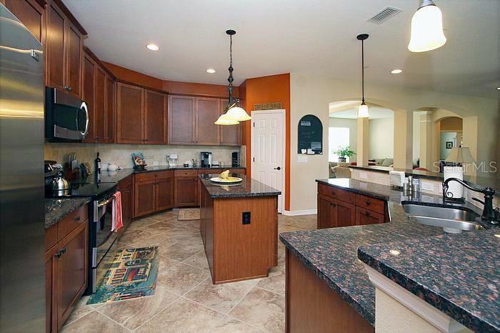 A kitchen features wood cabinets, granite countertops, a center island, and tile flooring — 1195 LATTIMORE DRIVE, CLERMONT, FL