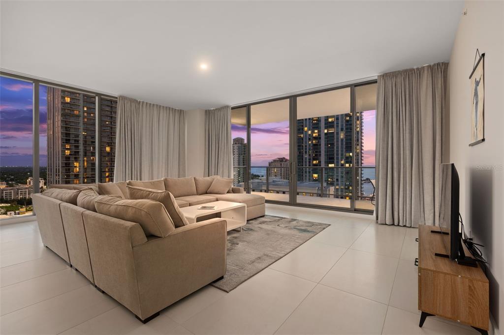 A modern living room features a large sectional sofa, floor-to-ceiling windows, and city skyline views — 275 1ST AVENUE S UNIT 1902, ST PETERSBURG, FL
