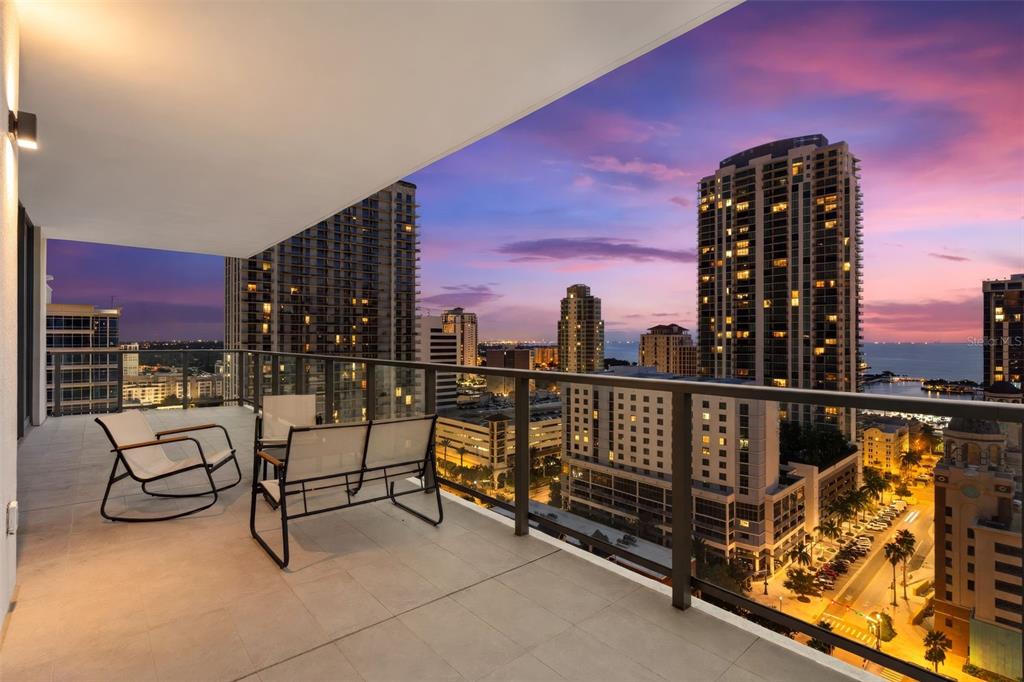 A balcony with outdoor furniture overlooks a city skyline and water at sunset — 275 1ST AVENUE S UNIT 1902, ST PETERSBURG, FL