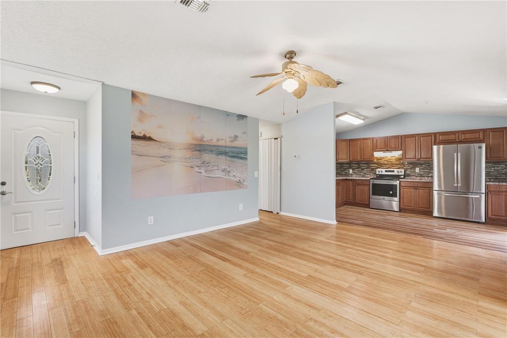 An open-concept living room with light wood flooring, a beach mural, and an adjacent kitchen — 14431 WORTHWHILE ROAD, PORT CHARLOTTE, FL