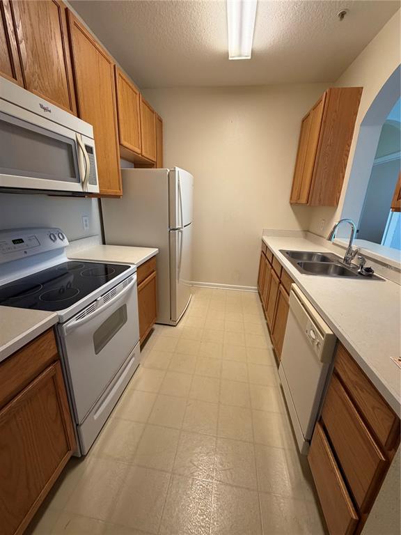 A galley kitchen features oak cabinets, white appliances, a double sink, and light-colored flooring — 6214 STEVENSON DRIVE UNIT 307, ORLANDO, FL
