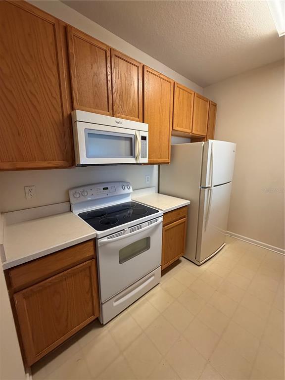 A kitchen features oak cabinets, white appliances, and light-colored countertops — 6214 STEVENSON DRIVE UNIT 307, ORLANDO, FL