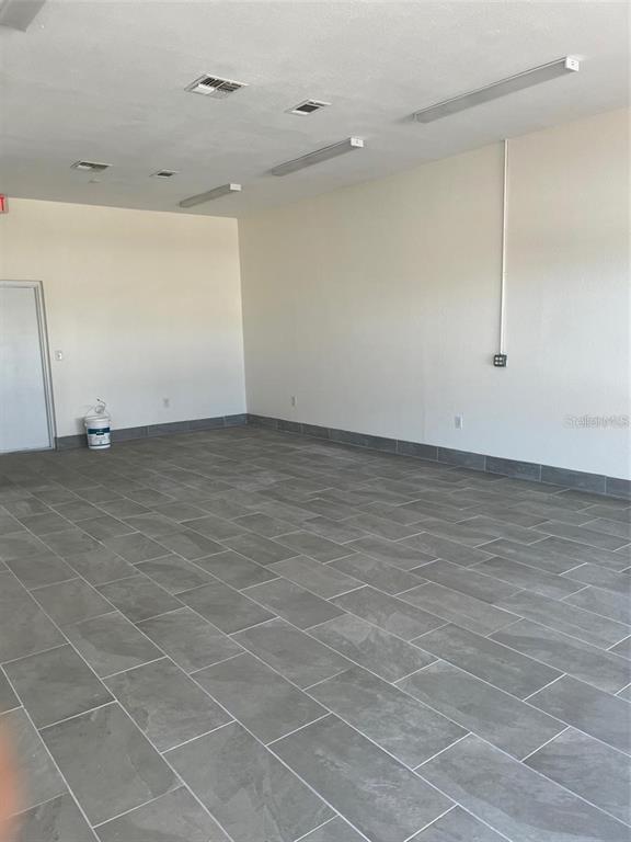 An empty room features gray tile flooring, white walls, and rectangular ceiling light fixtures — 119 TAMIAMI TRAIL UNIT G, PORT CHARLOTTE, FL