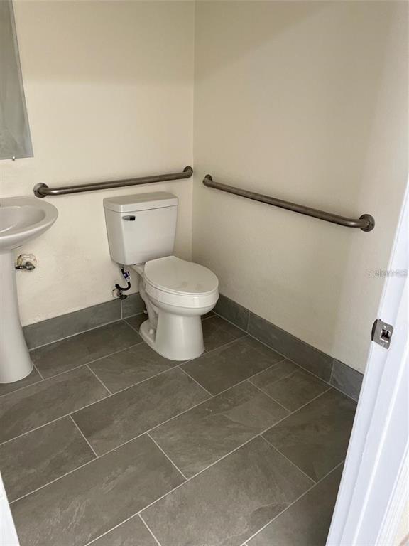 A bathroom features a white toilet, a pedestal sink, and grab bars on the walls — 119 TAMIAMI TRAIL UNIT G, PORT CHARLOTTE, FL