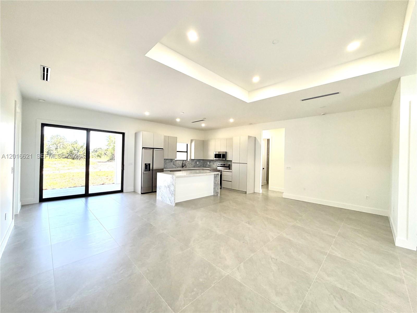 A modern kitchen with white cabinets and a marble island opens to a living area — 3522 Randall Blvd, Naples FL 34120, NAPLES, FL
