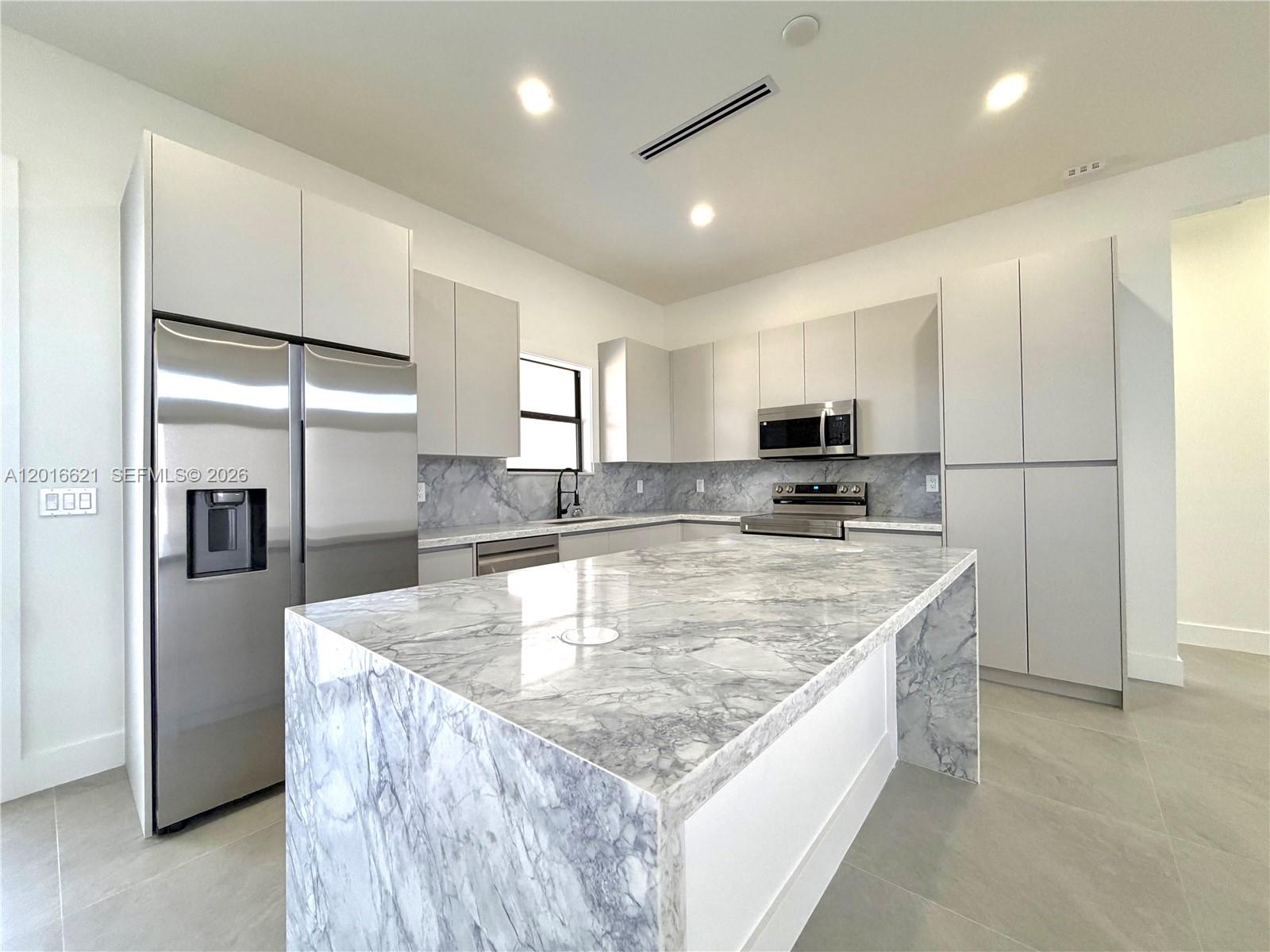 A modern kitchen features a marble waterfall island, stainless steel appliances, and light gray cabinetry — 3522 Randall Blvd, Naples FL 34120, NAPLES, FL