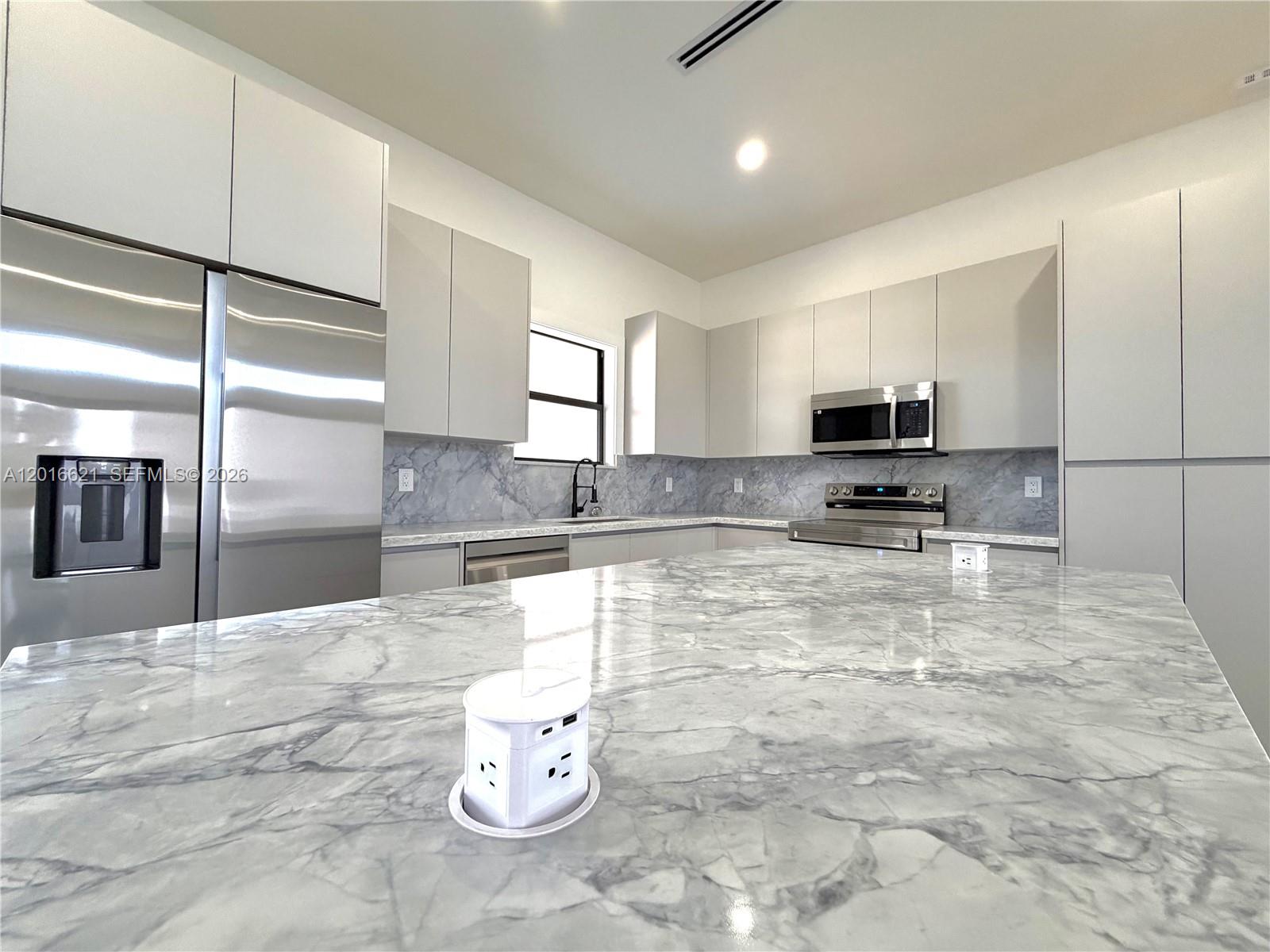 A modern kitchen features a large marble island with a pop-up power outlet — 3522 Randall Blvd, Naples FL 34120, NAPLES, FL