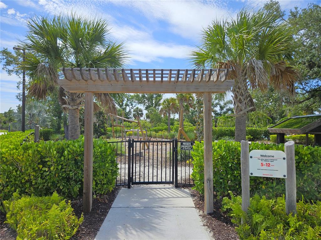 A wooden pergola stands over a gated entrance leading to a fenced outdoor playground area — 15285 SHADY PALMS LANE, NOKOMIS, FL