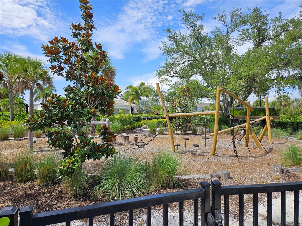 A playground with wooden climbing structures and a rope net sits behind a black fence — 15285 SHADY PALMS LANE, NOKOMIS, FL