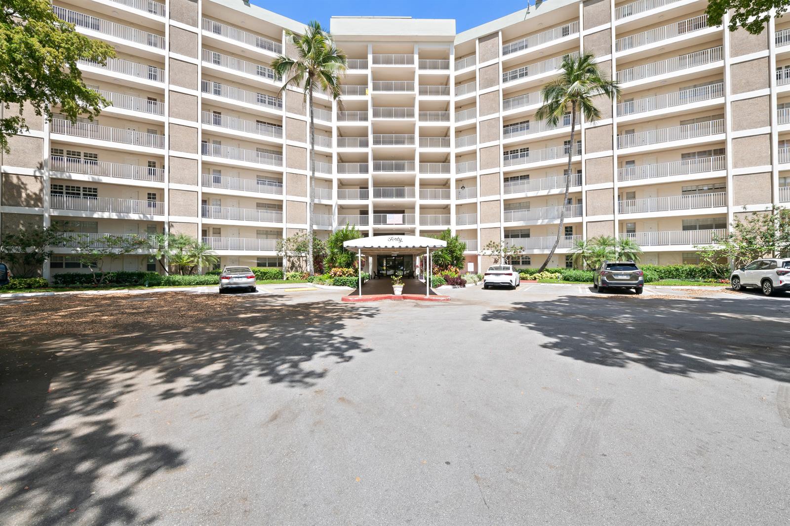 A multi-story residential building features a central entrance canopy and a paved parking area — 3051 N Course Drive # 211, Pompano Beach FL 33069, POMPANO BEACH, FL