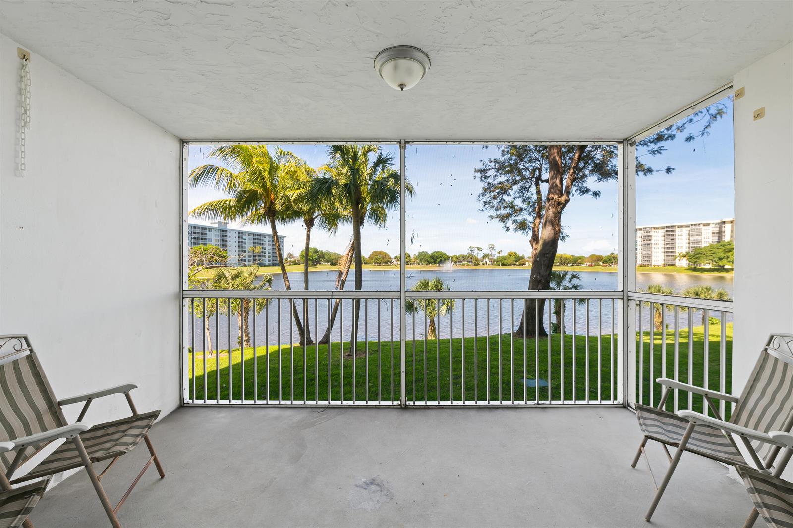 A screened-in balcony features two folding chairs overlooking a lake and palm trees — 3051 N Course Drive # 211, Pompano Beach FL 33069, POMPANO BEACH, FL