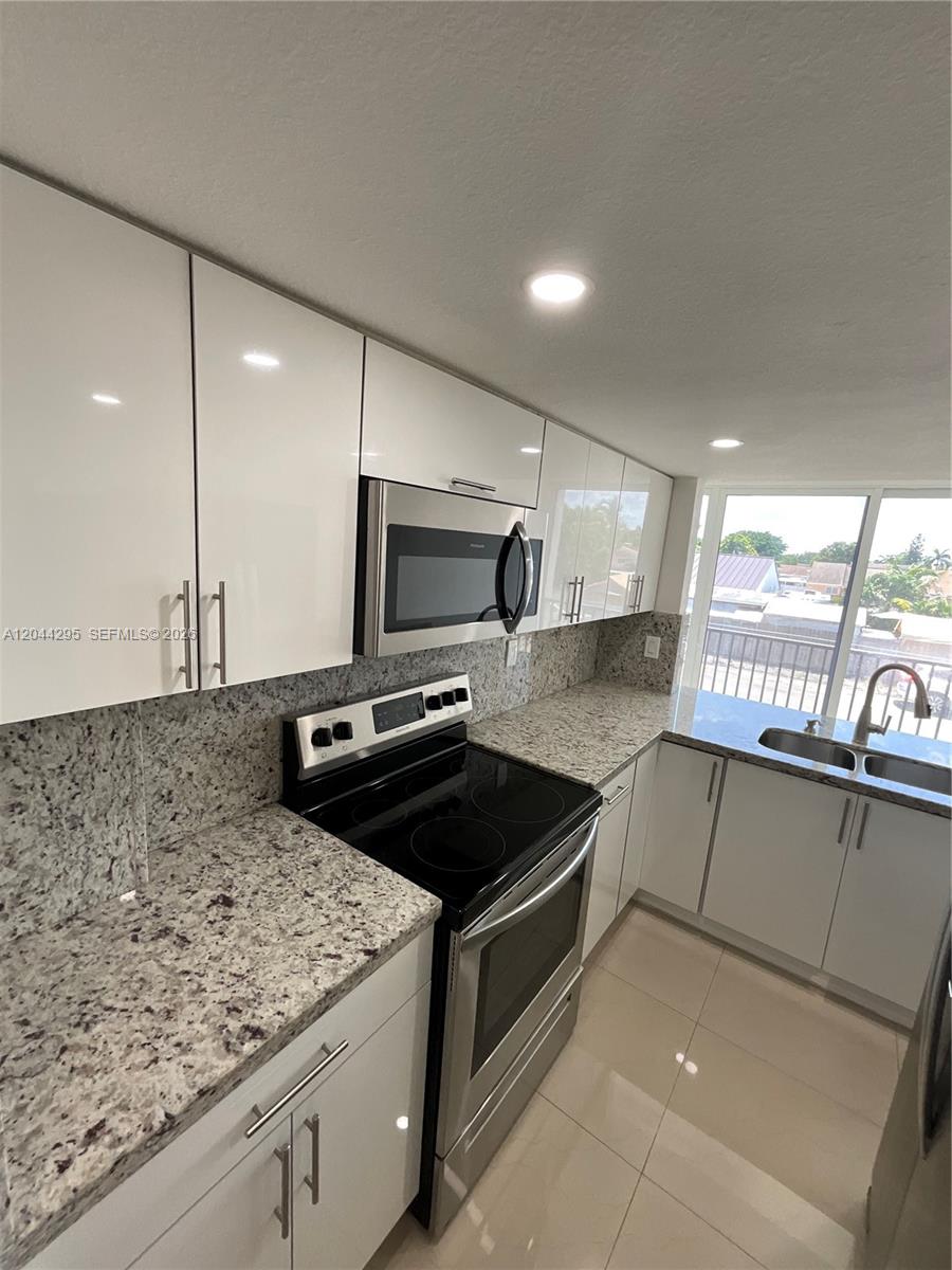A modern kitchen features white glossy cabinets, granite countertops, and stainless steel appliances — 9441 SW 4th St # 214, Miami FL 33174, MIAMI, FL