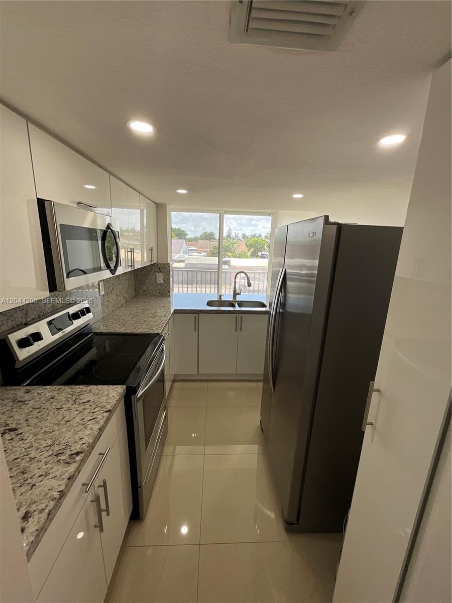 A galley kitchen features white cabinets, stainless steel appliances, and granite countertops — 9441 SW 4th St # 214, Miami FL 33174, MIAMI, FL